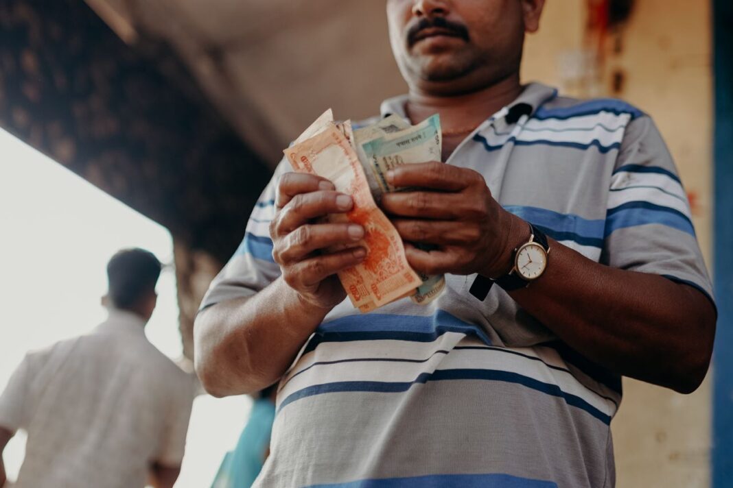 India inflation likely rose to 4.1% in May: Mint poll Man in Indian market counting rupee notes, showcasing daily street commerce.