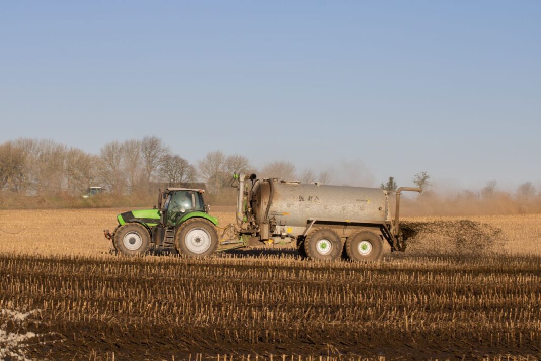 Fertilizer subsidy set to zoom, but govt may stay off supplementary demands A tractor with a tanker spreading fertilizer over a barren farmland under clear skies.