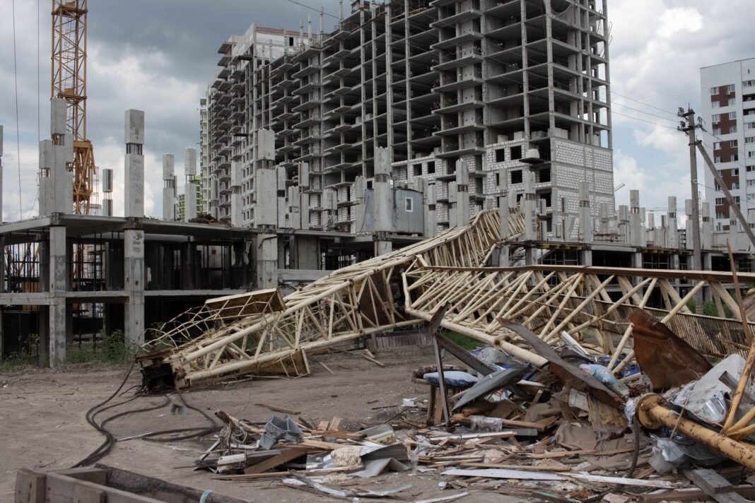 Four killed, two injured as speeding dumper truck slams into Delhi crane during CCTV installation work An urban construction site featuring a collapsed crane and unfinished buildings under cloudy skies.