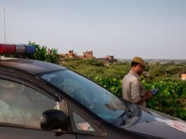 Police officer using tablet beside patrol car in scenic outdoor setting.