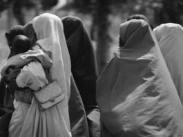 Group of women in traditional attire walking outdoors, captured in black and white.