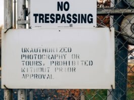 A warning sign on a metal fence prohibiting trespassing and unauthorized activities.