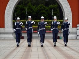 Five uniformed military personnel marching in formation during a ceremonial parade outdoors.
