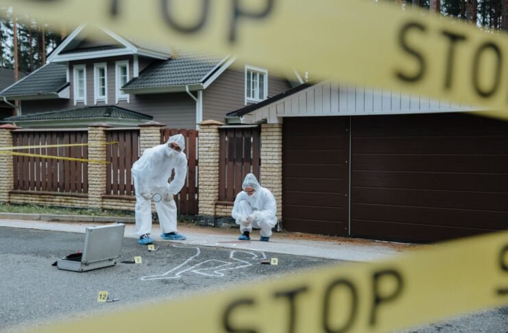 Forensic team examining crime scene with chalk outline and evidence markers outdoors.